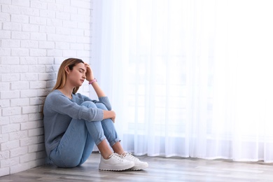 Emotional teenage girl sitting on floor indoors. Space for text