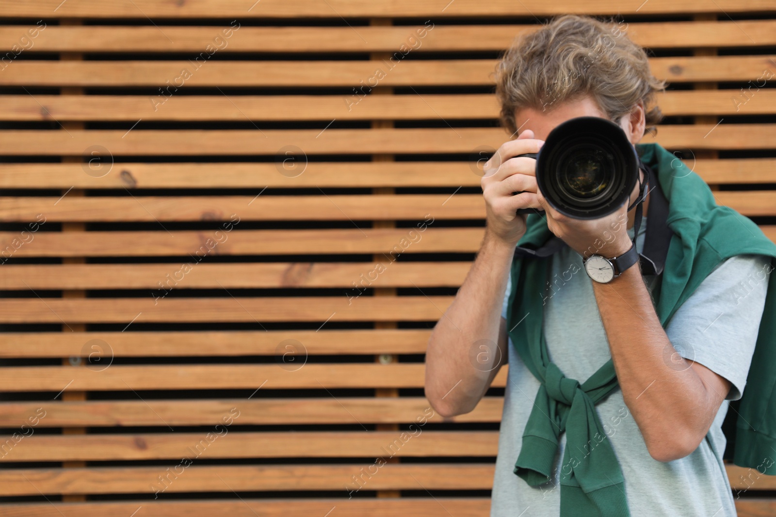 Photo of Young male photographer with professional camera near wooden wall. Space for text