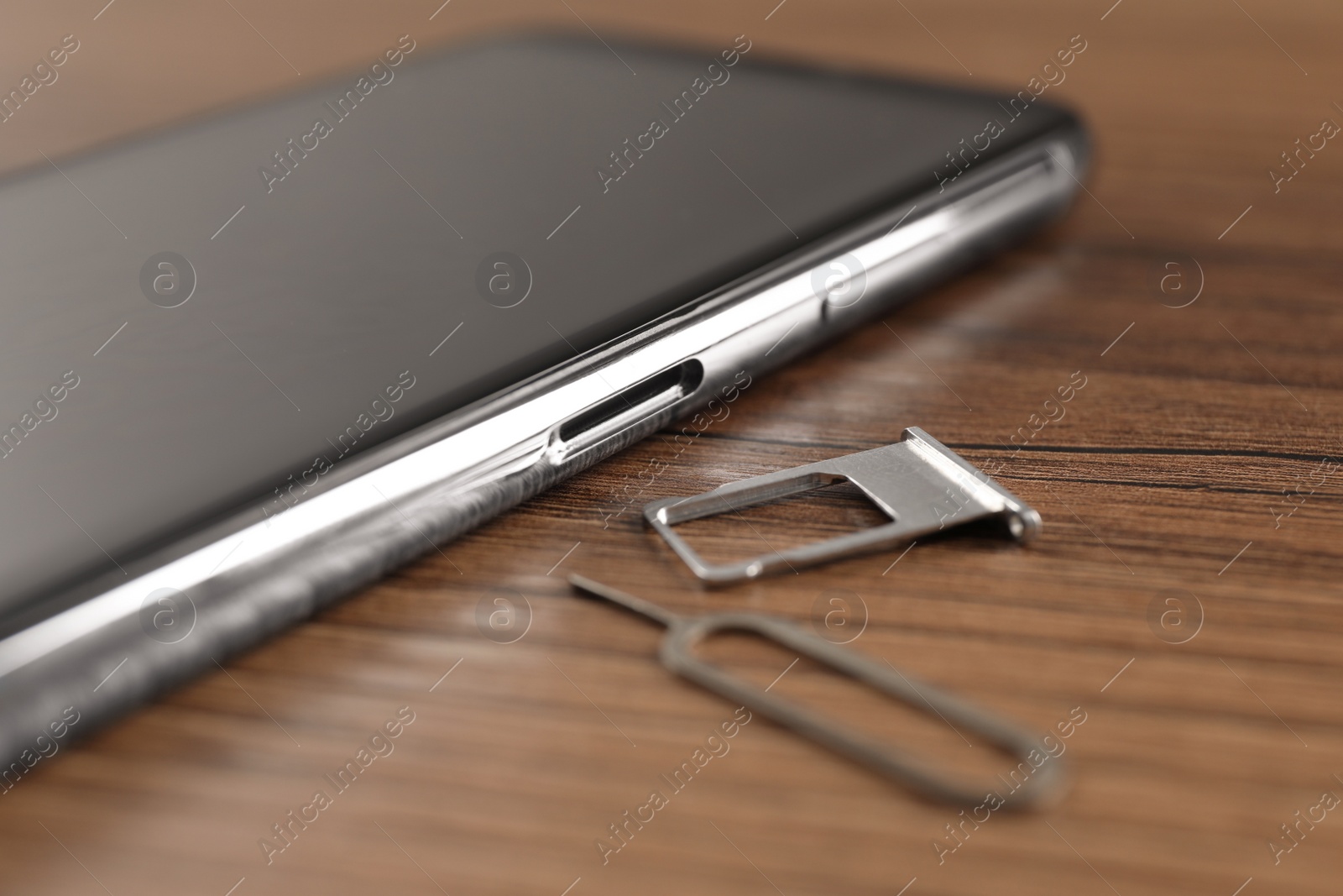 Photo of SIM card tray, mobile phone and ejector tool on wooden table, closeup