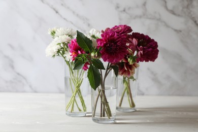 Bouquet of beautiful wild flowers and leaves in vases on white wooden table against marble background