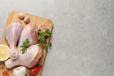 Photo of Wooden board with fresh raw chicken legs and other products on light grey table, top view. Space for text