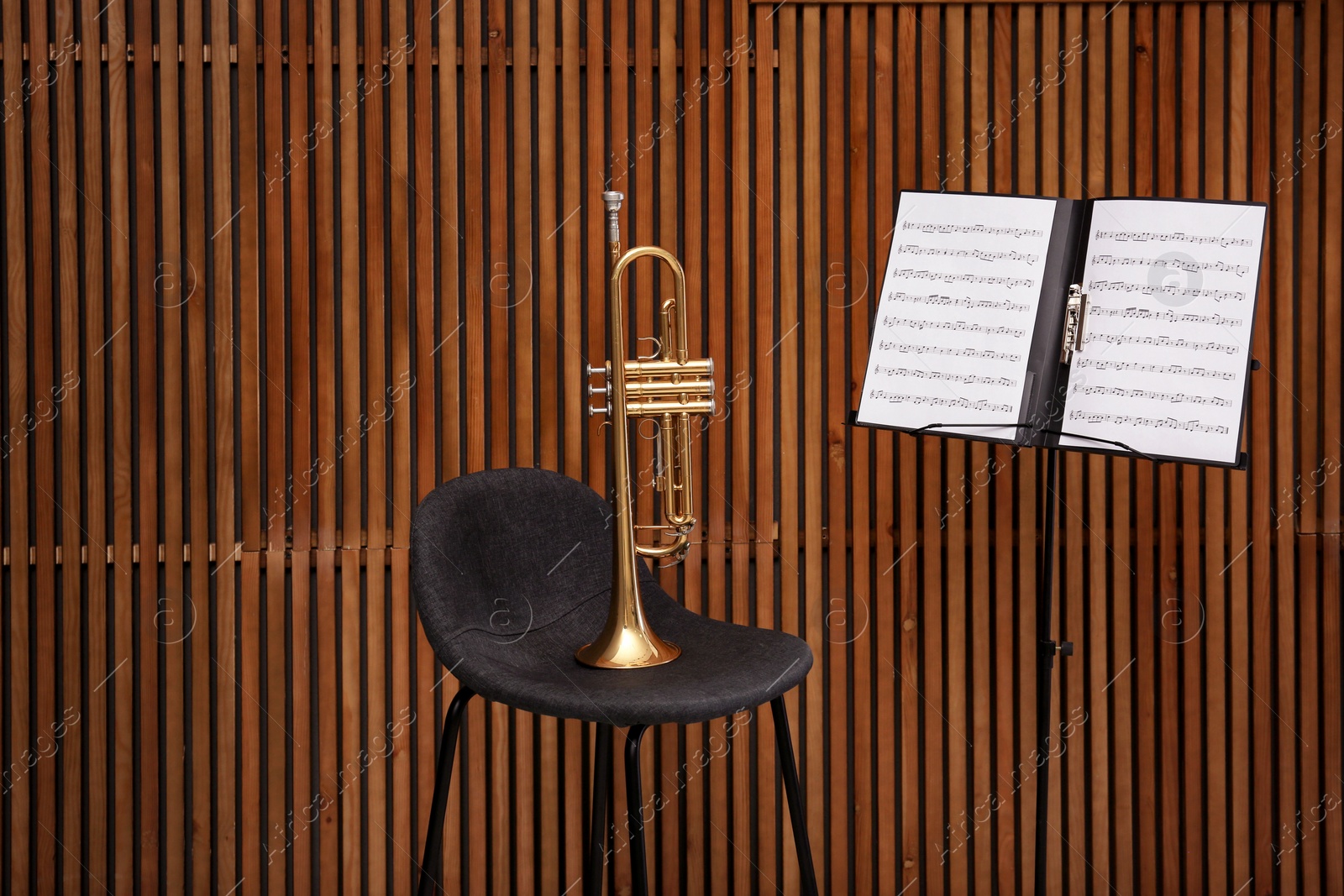 Photo of Trumpet, chair and note stand with music sheets on wooden wall background