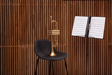 Photo of Trumpet, chair and note stand with music sheets on wooden wall background