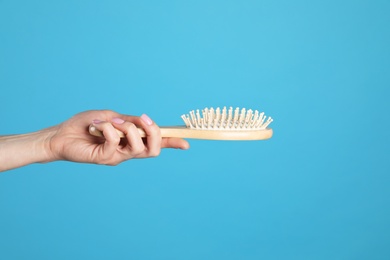 Photo of Woman holding wooden hair brush against blue background, closeup