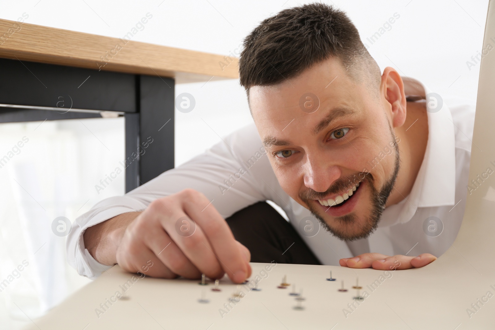 Photo of Man putting pins on chair in office. April fool's day