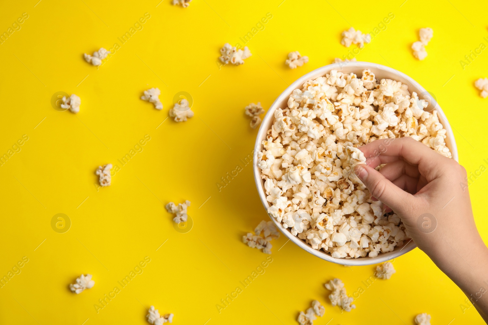 Photo of Woman taking fresh pop corn from bucket on yellow background, top view