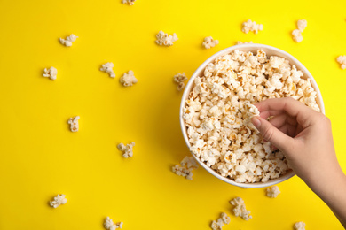 Woman taking fresh pop corn from bucket on yellow background, top view