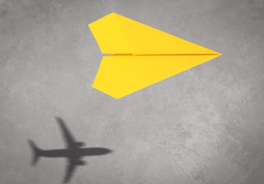 Image of Flying paper plane and shadow of a real airplane on grey background