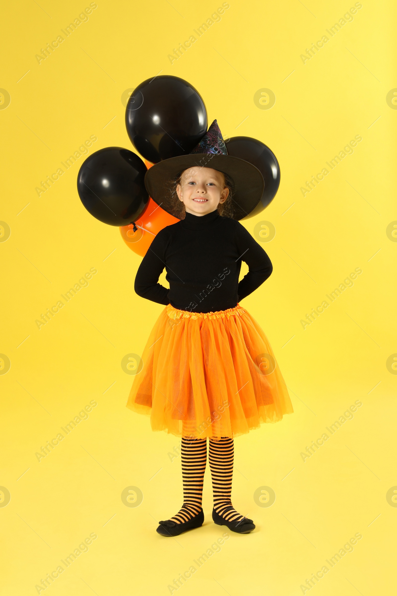 Photo of Cute little girl with balloons wearing Halloween costume on yellow background