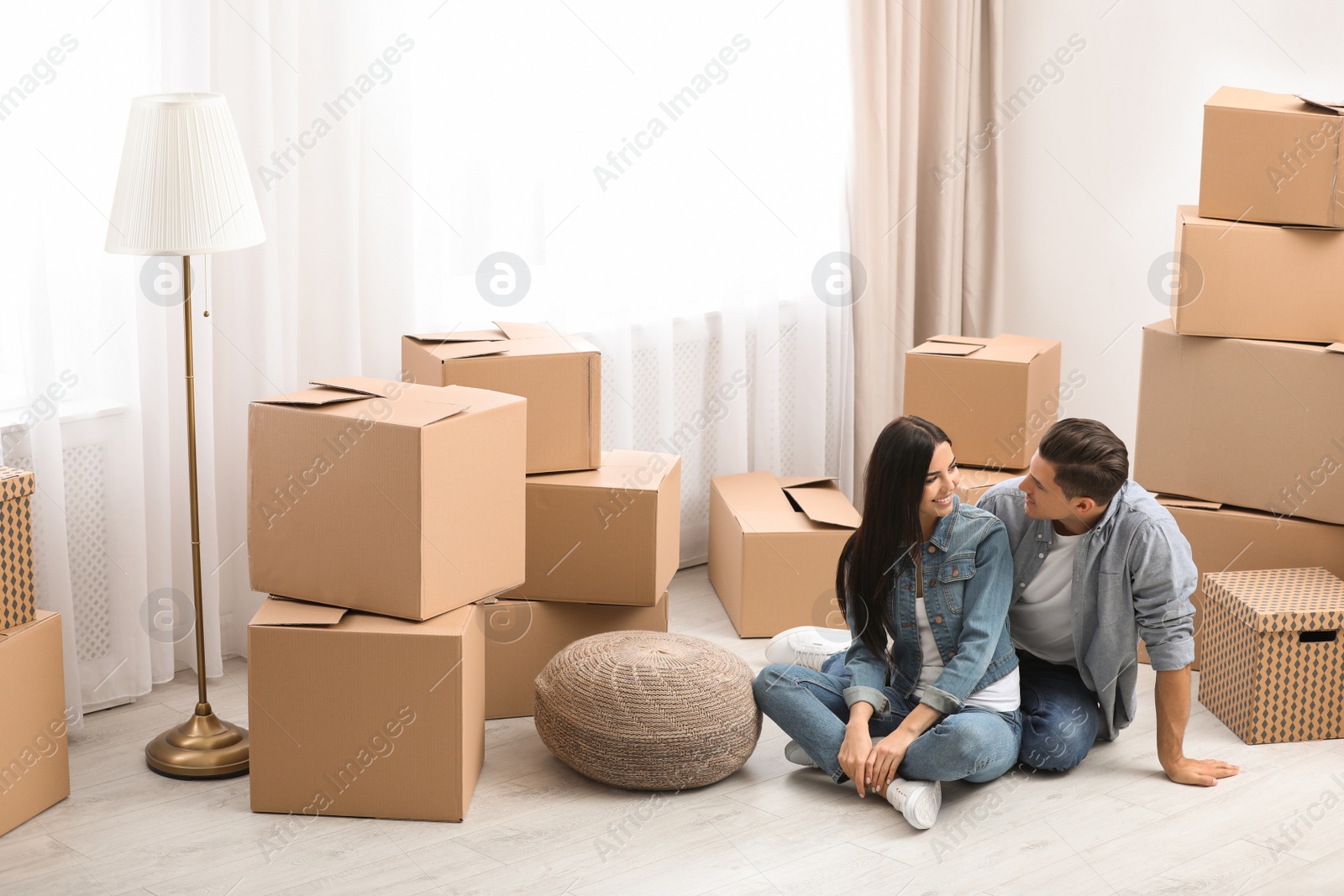 Photo of Happy couple in room with cardboard boxes on moving day