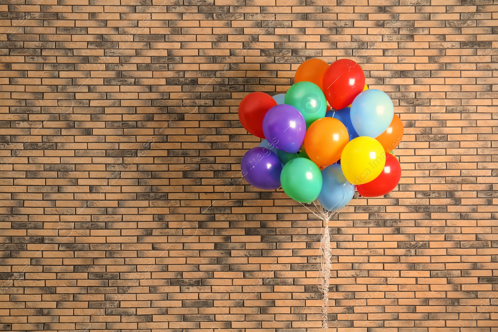 Photo of Bunch of bright balloons and space for text against brick wall