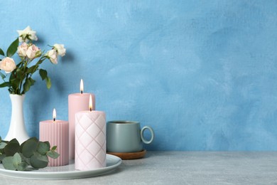 Photo of Scented candles, flowers and cup on grey table near light blue wall, space for text