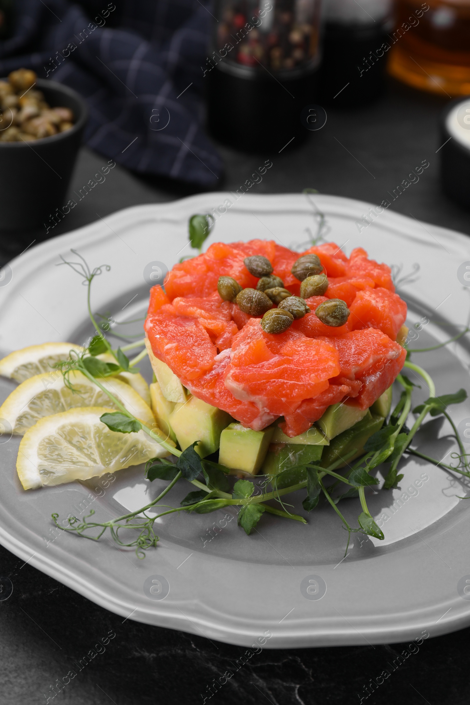 Photo of Delicious salmon tartare served with avocado and lemon on dark table, closeup