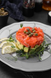 Photo of Delicious salmon tartare served with avocado and lemon on dark table, closeup