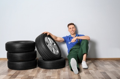 Male mechanic with car tires on light wall background