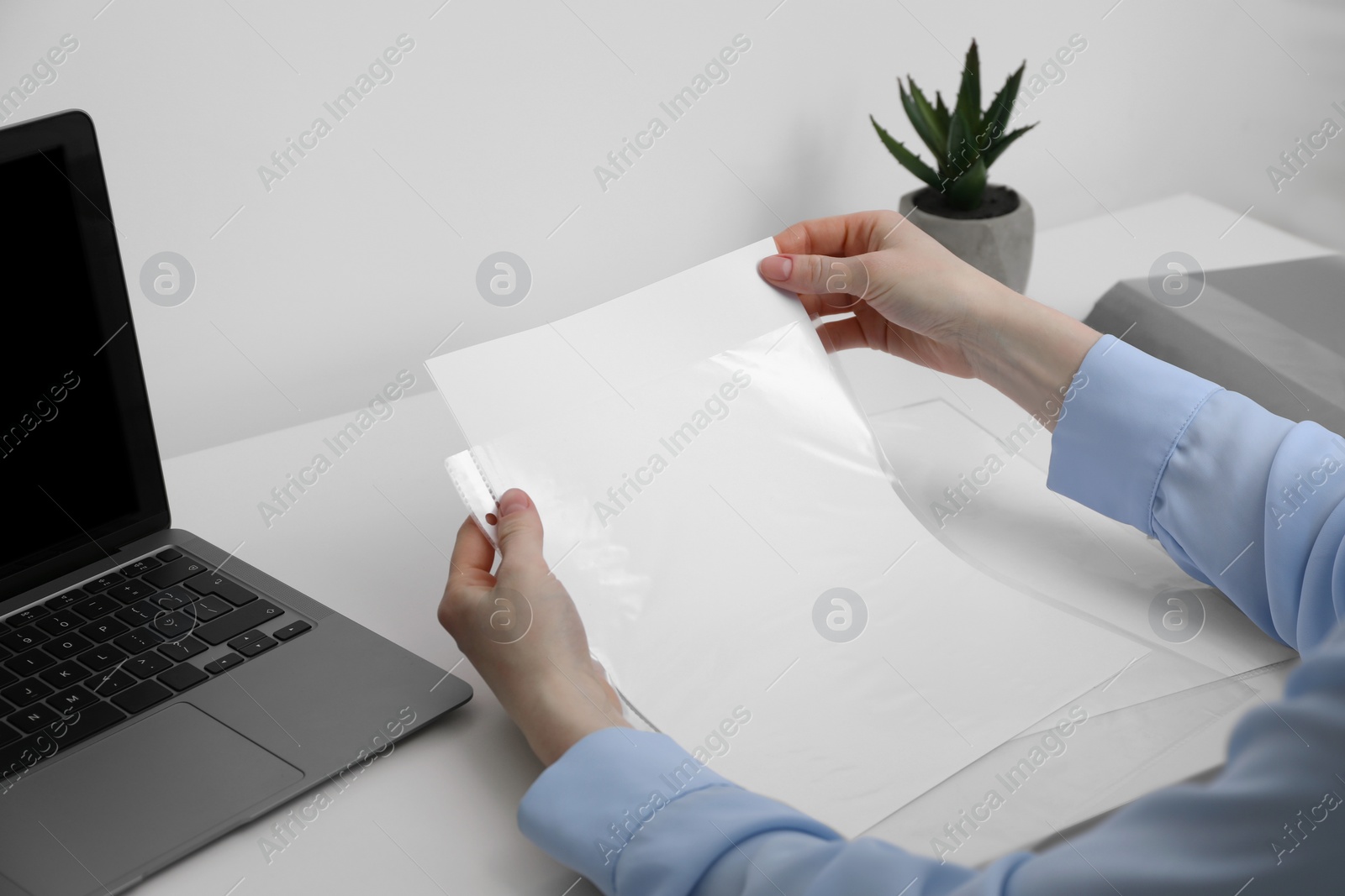 Photo of Woman putting paper sheet into punched pocket at white table, closeup