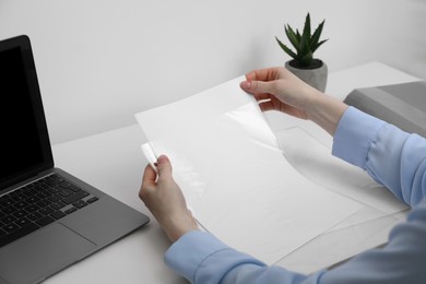 Woman putting paper sheet into punched pocket at white table, closeup