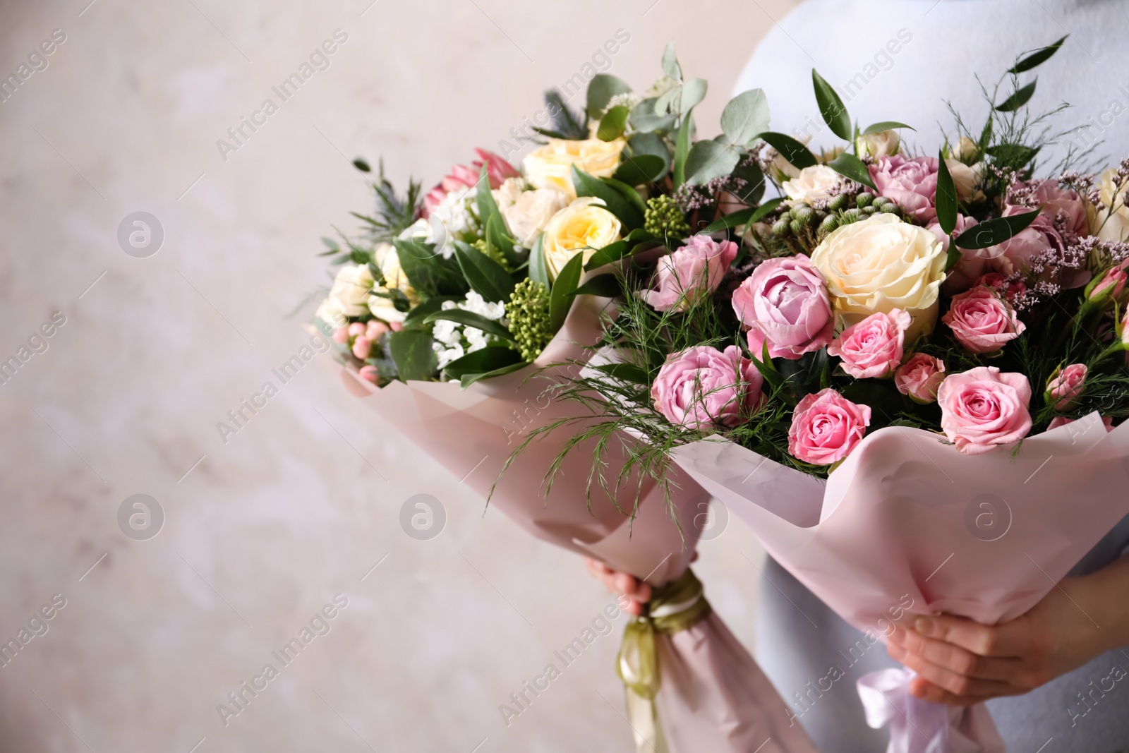 Photo of Woman with bouquets of beautiful flowers on beige background, closeup