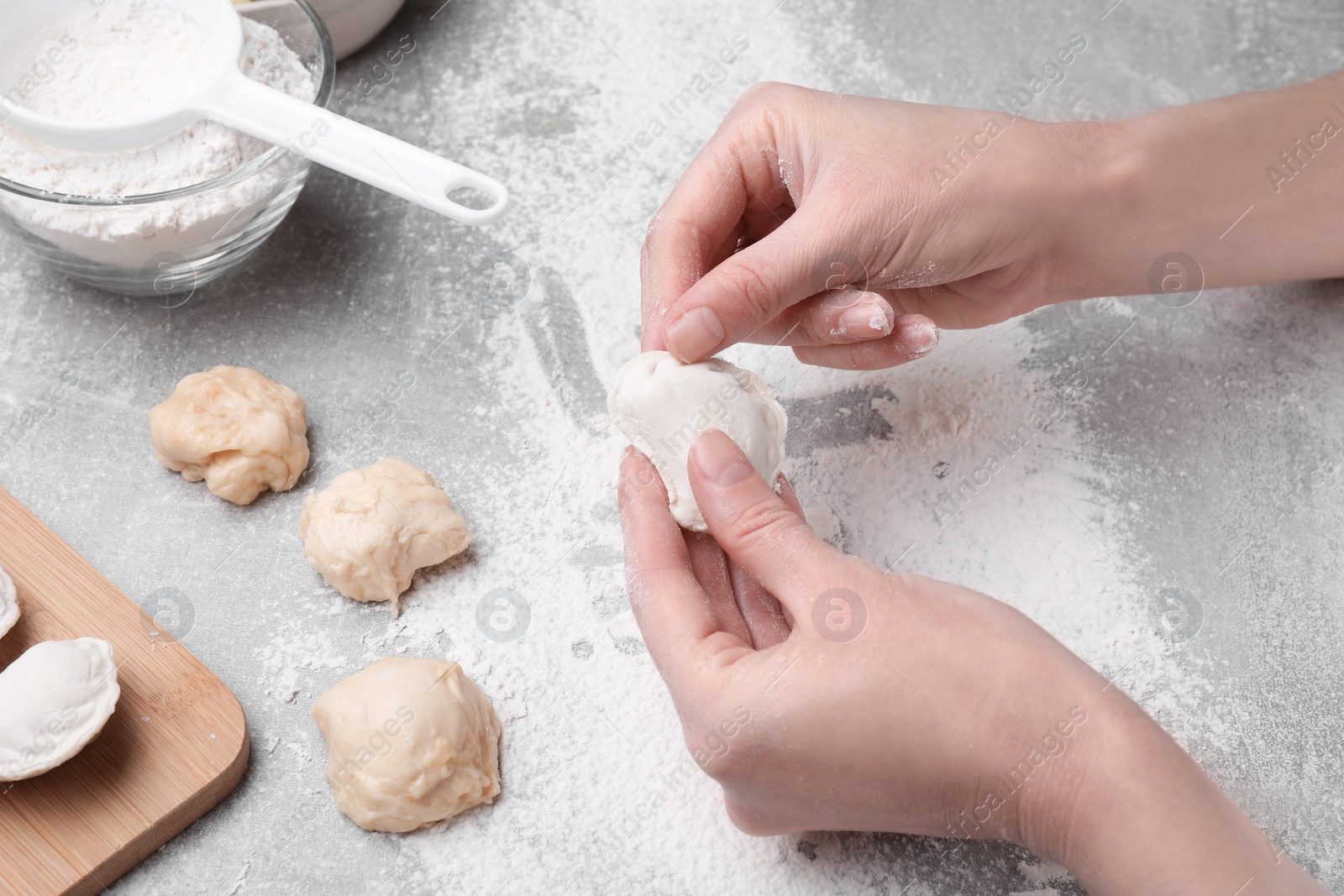 Photo of Woman making dumplings (varenyky) at grey table, closeup