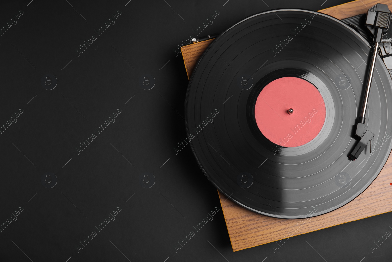 Photo of Modern vinyl record player with disc on black background, top view. Space for text