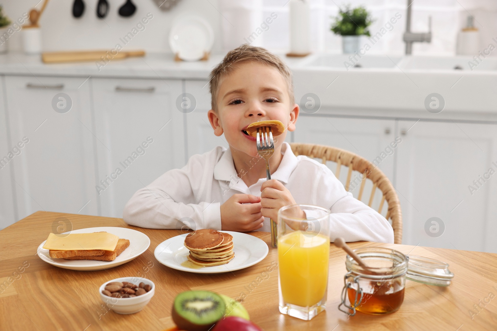 Photo of Breakfast time. Cute little boy eating pancakes at table in kitchen