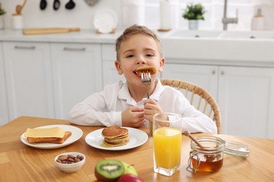 Photo of Breakfast time. Cute little boy eating pancakes at table in kitchen