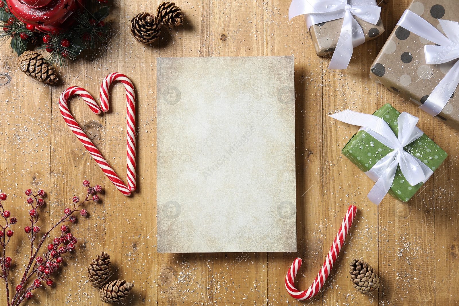 Photo of Flat lay composition with blank paper sheet, candy canes and Christmas decor on wooden table, space for text. Letter to Santa