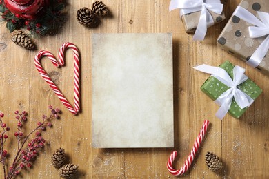 Flat lay composition with blank paper sheet, candy canes and Christmas decor on wooden table, space for text. Letter to Santa
