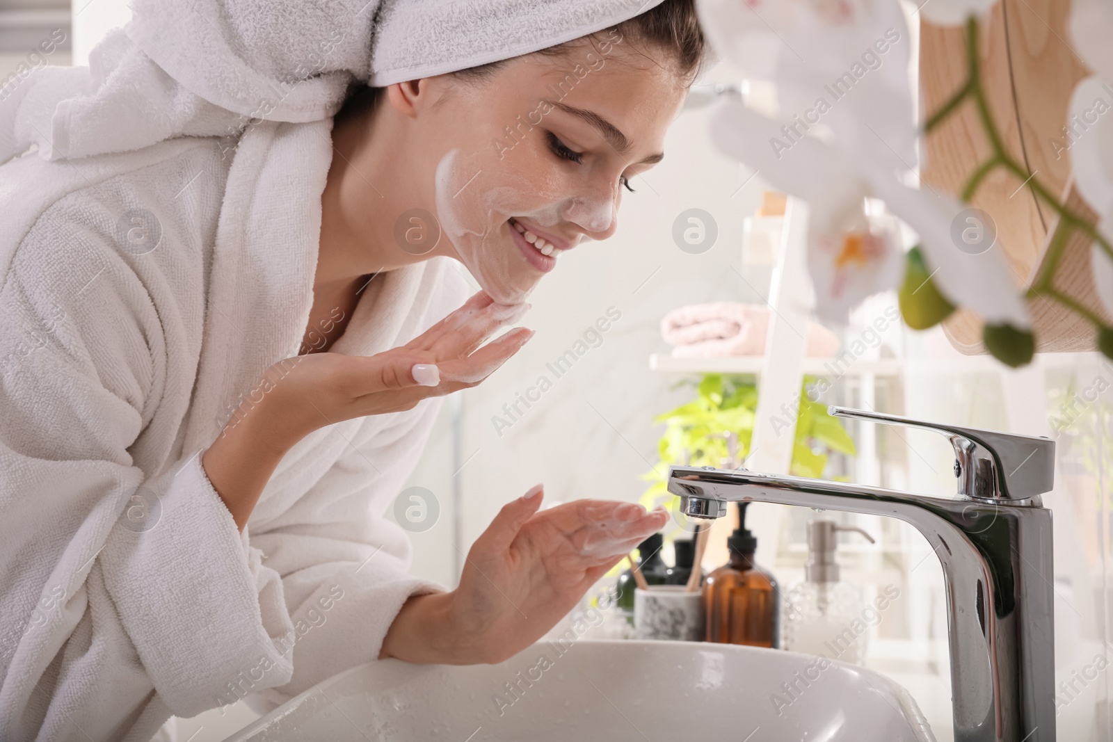 Photo of Beautiful teenage girl applying cleansing foam onto face in bathroom. Skin care cosmetic