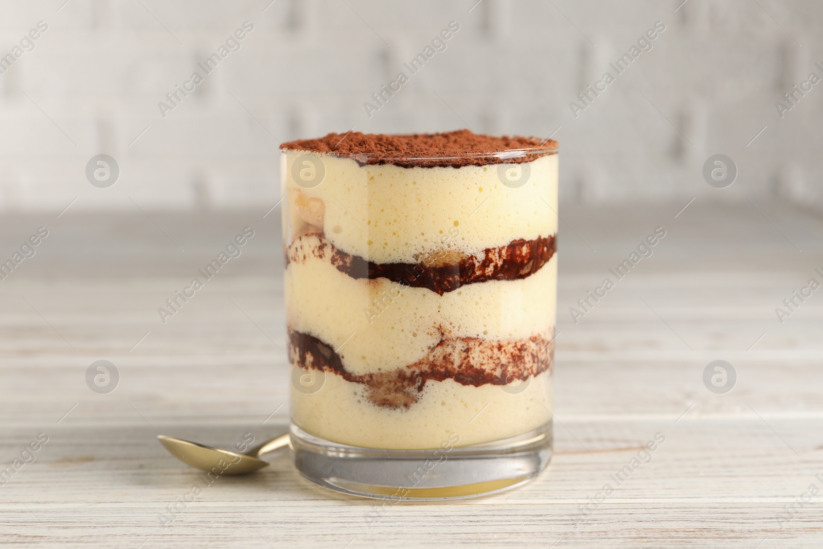 Photo of Delicious tiramisu in glass on light wooden table, closeup