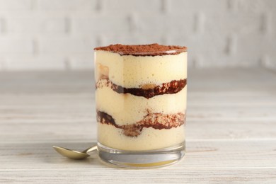 Photo of Delicious tiramisu in glass on light wooden table, closeup