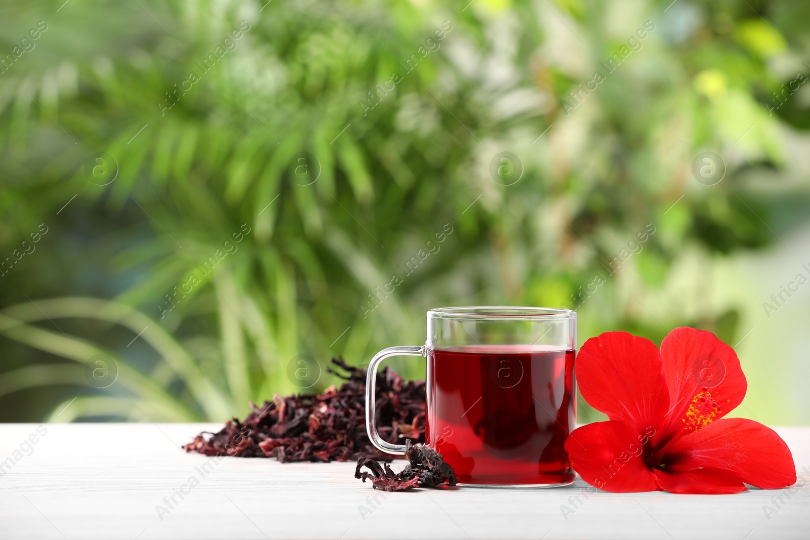 Photo of Delicious hibiscus tea and flowers on white wooden table outdoors, space for text