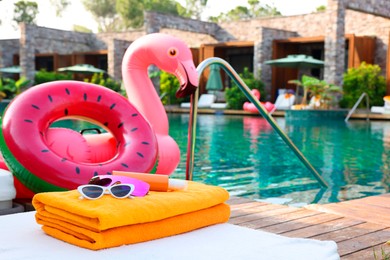 Beach accessories on sun lounger, inflatable ring and float near outdoor swimming pool at luxury resort, selective focus. Space for text