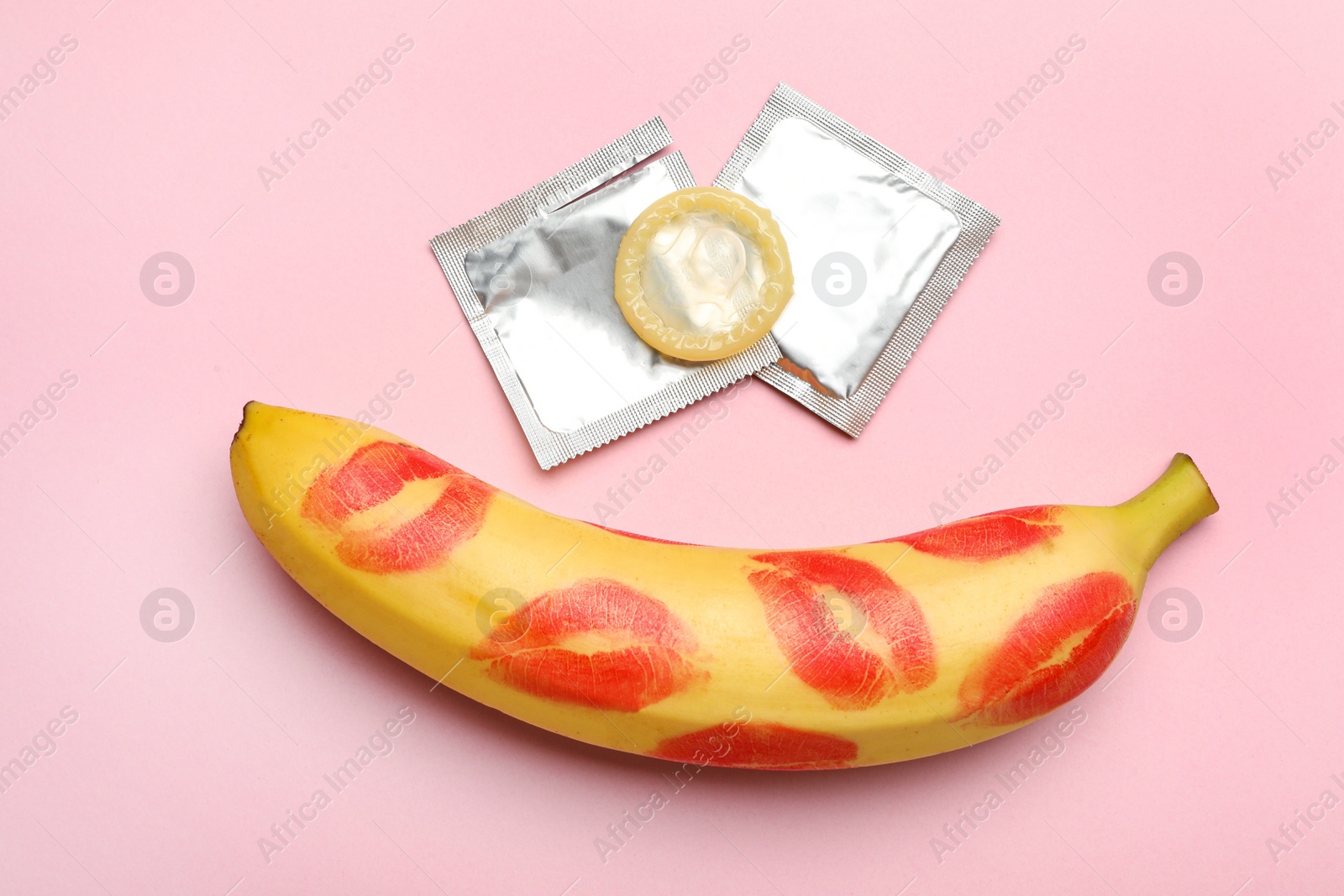 Photo of Condoms and banana with lipstick kiss marks on pink background, flat lay. Safe sex