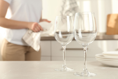 Photo of Woman wiping plate with towel in kitchen, focus on clean glasses