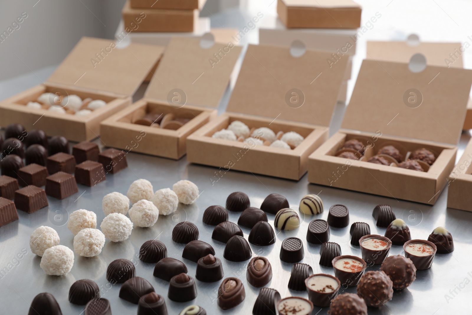 Photo of Different delicious chocolate candies and boxes on white table. Production line