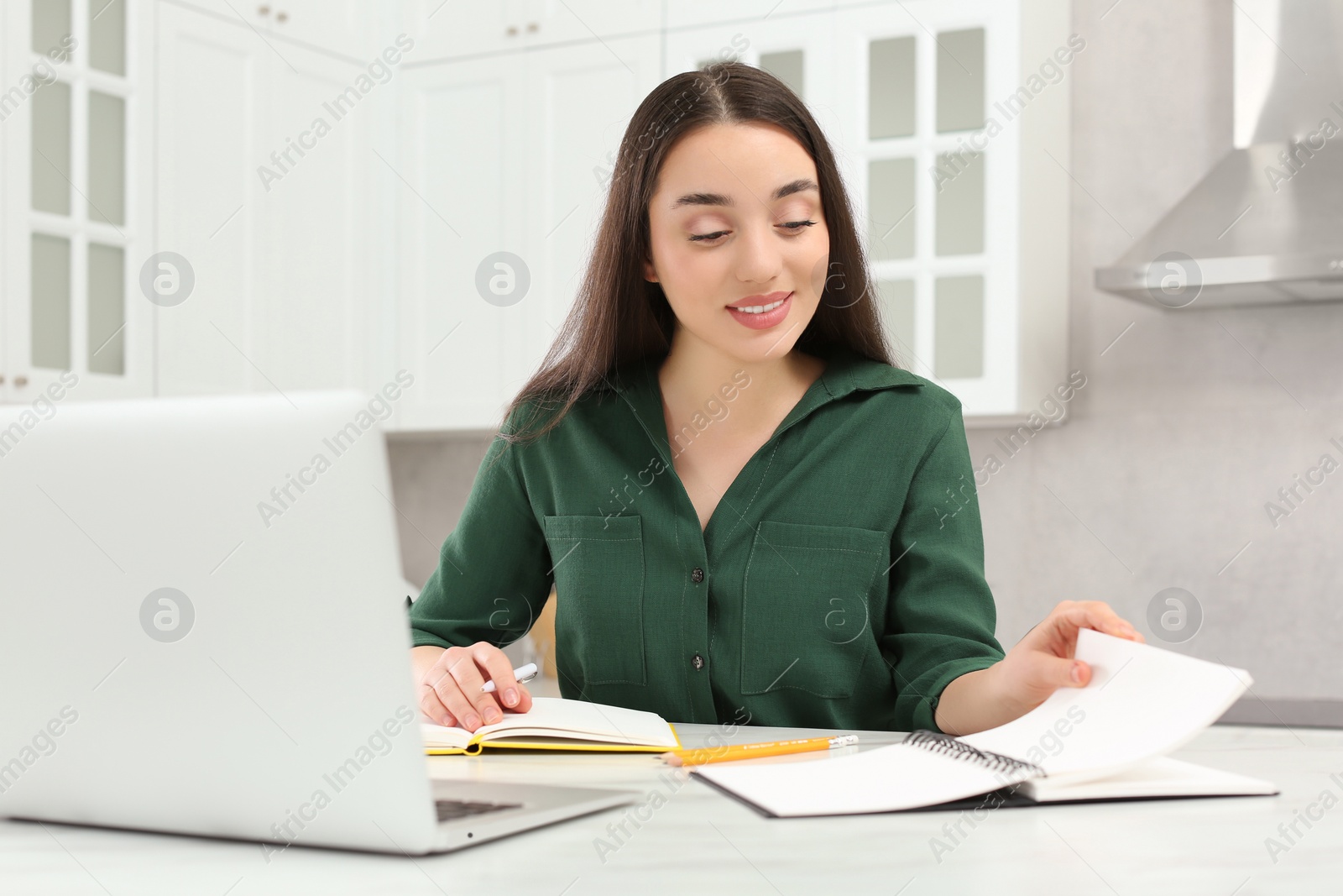 Photo of Home workplace. Woman looking at notebook near laptop at marble desk in kitchen