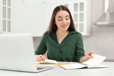 Home workplace. Woman looking at notebook near laptop at marble desk in kitchen