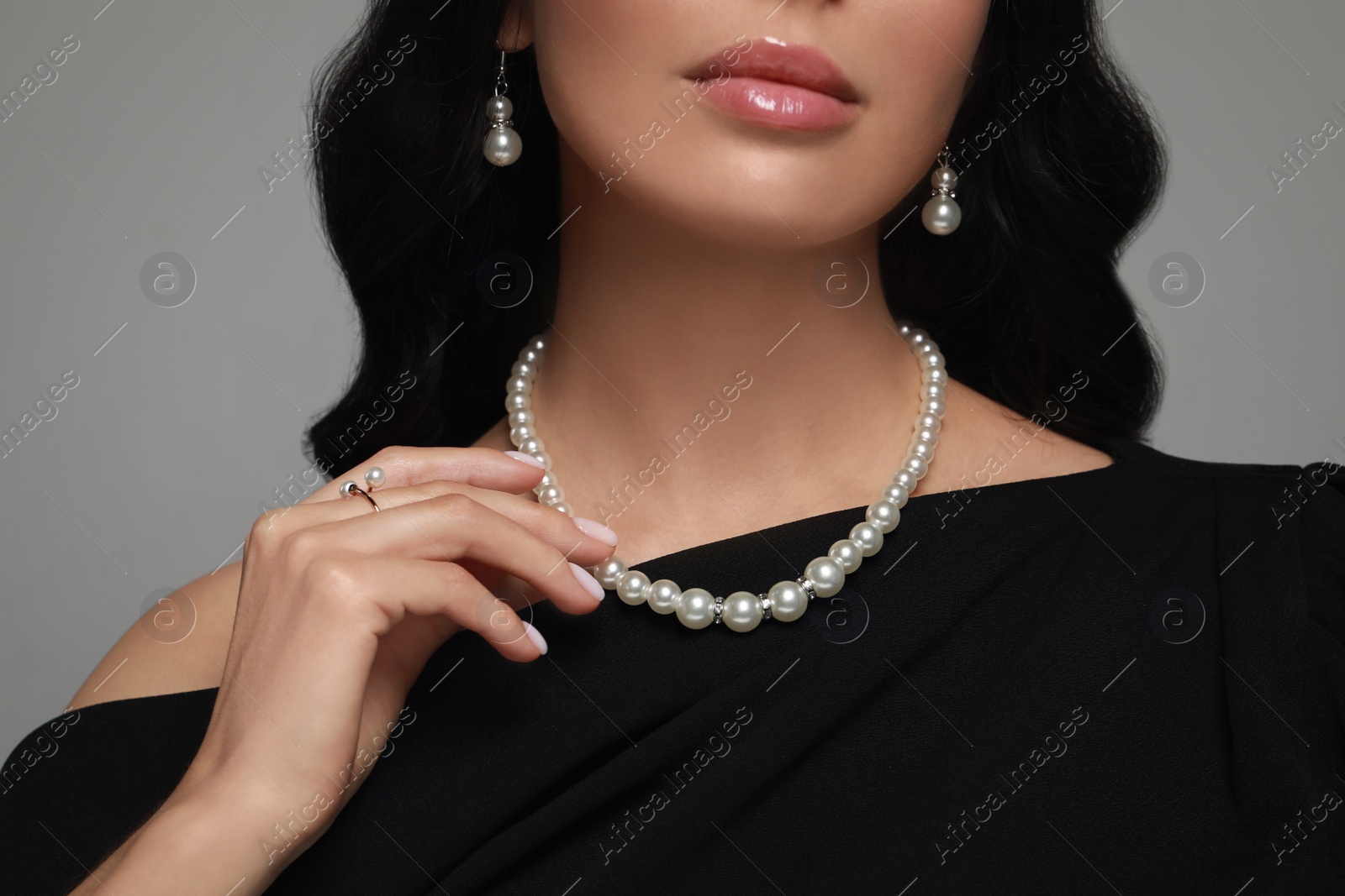 Photo of Young woman wearing elegant pearl jewelry on grey background, closeup