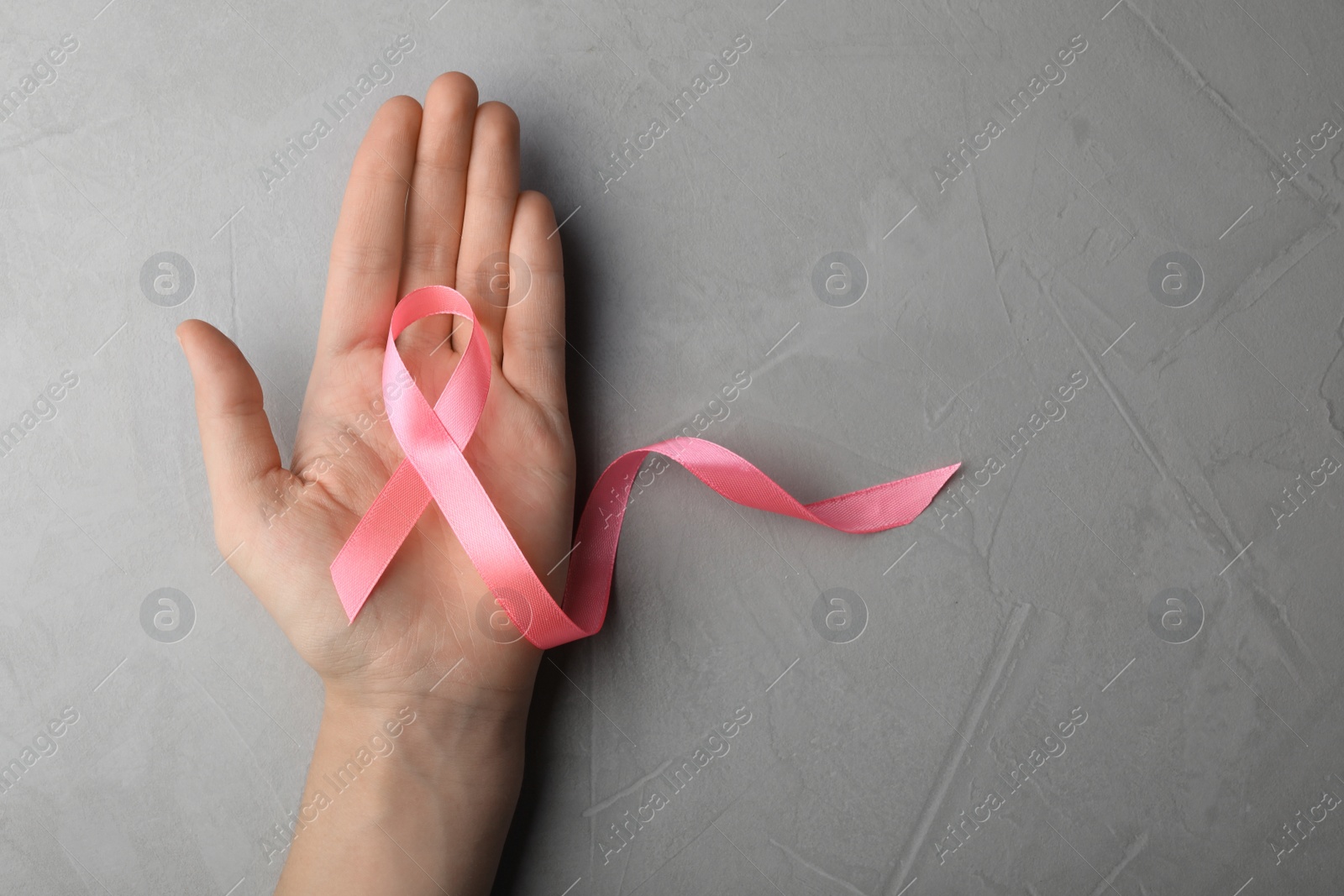 Photo of Woman holding pink ribbon on grey background, top view with space for text. Breast cancer awareness concept