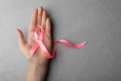 Photo of Woman holding pink ribbon on grey background, top view with space for text. Breast cancer awareness concept