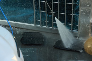 Photo of Cleaning auto mats with high pressure water jet at car wash, closeup
