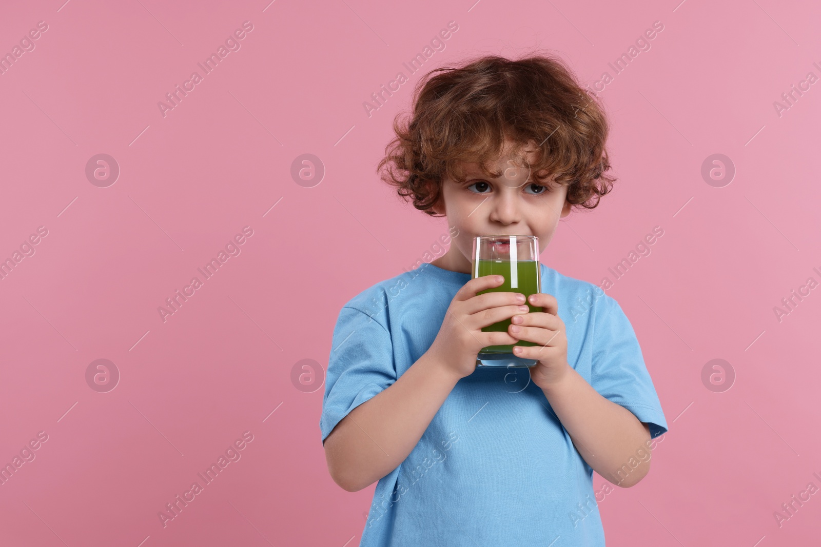 Photo of Cute little boy drinking fresh juice on pink background, space for text