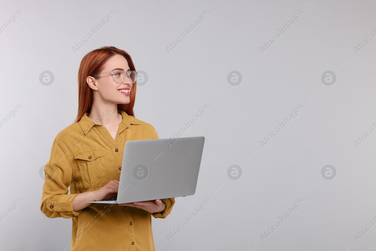 Photo of Smiling young woman working with laptop on grey background, space for text