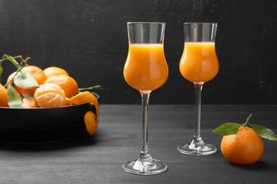 Tasty tangerine liqueur in glasses and fresh fruits on black wooden table