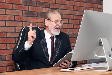 Happy senior boss having online meeting via computer at wooden table in office