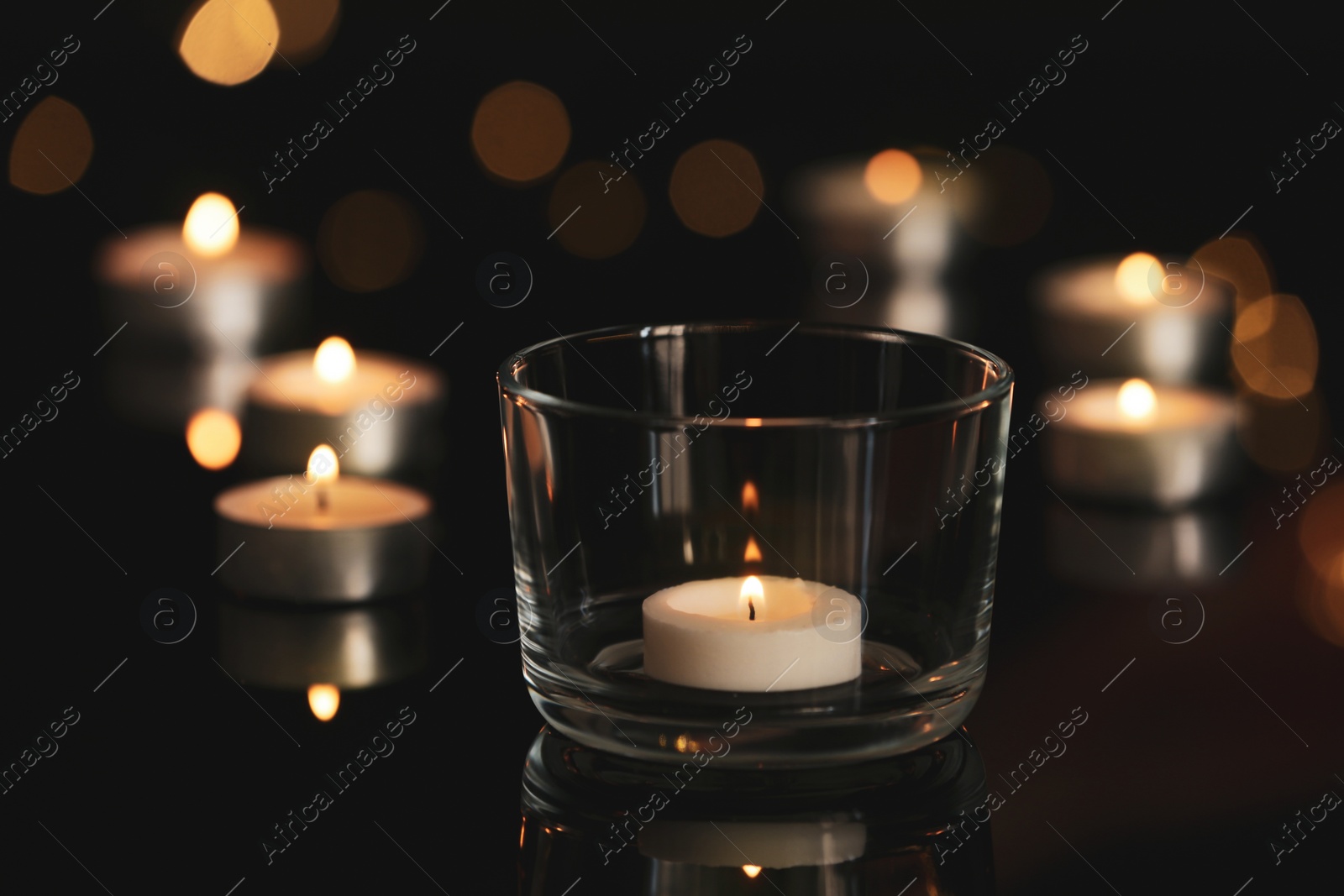 Photo of Wax candles burning on table in darkness, closeup