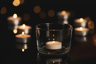 Wax candles burning on table in darkness, closeup