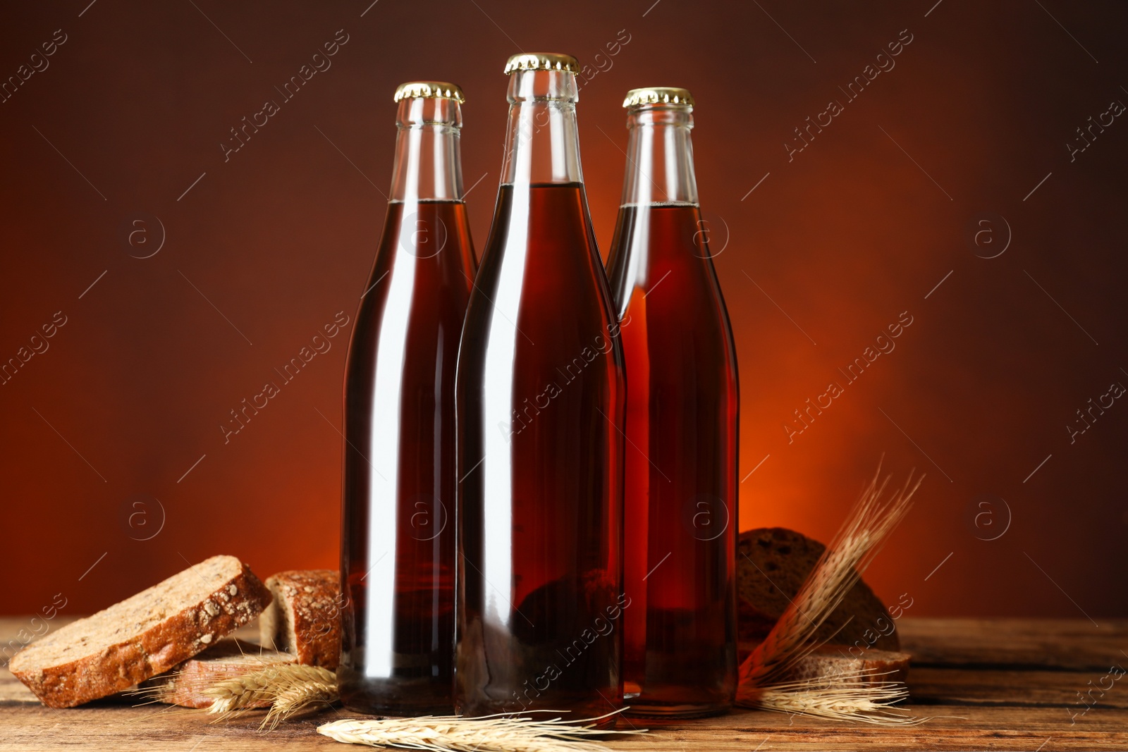 Photo of Bottles of delicious fresh kvass, spikelets and bread on wooden table