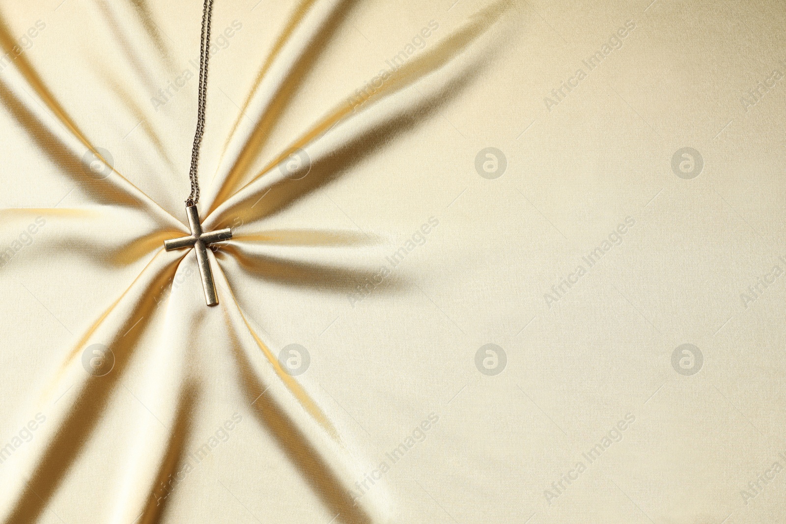 Photo of One cross with chain on golden cloth, top view and space for text. Religion of Christianity